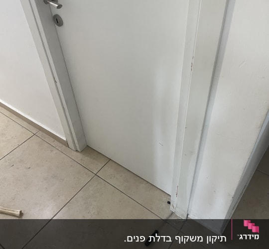 דלת לבנה עם ידית מתכת ומברג על הרצפה